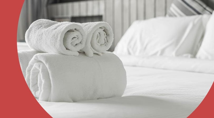 Fresh rolled white towels on a neatly made bed.