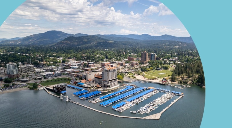 Aerial view of Coeur d'Alene's lakefront downtown with its marina and forested mountains beyond.