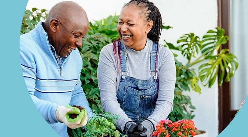 A 55+ couple smiling while gardening in their backyard.