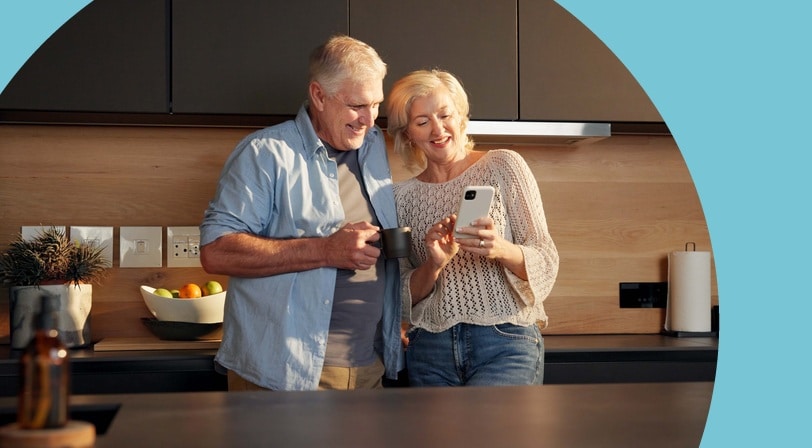 A smiling mature couple checking a phone together in a modern kitchen, enjoying a relaxed moment at home.