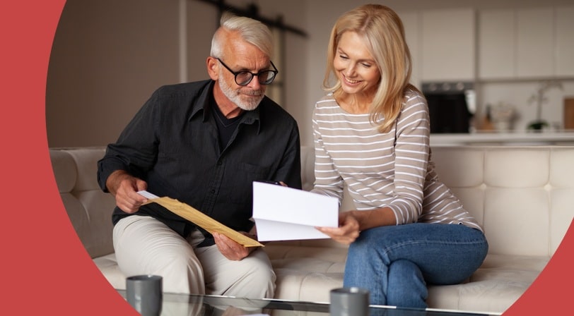 A couple sits together on their couch reviewing paperwork and a letter about their 55+ community home inspection.