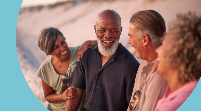 Four 55+ friends laughing together outdoors near sand dunes at golden hour.