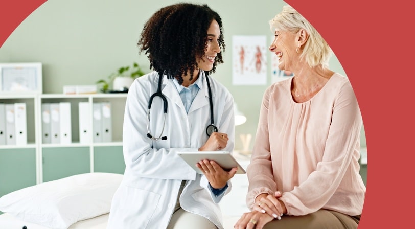 A doctor with a tablet talking with a smiling 55+ patient in an exam room.