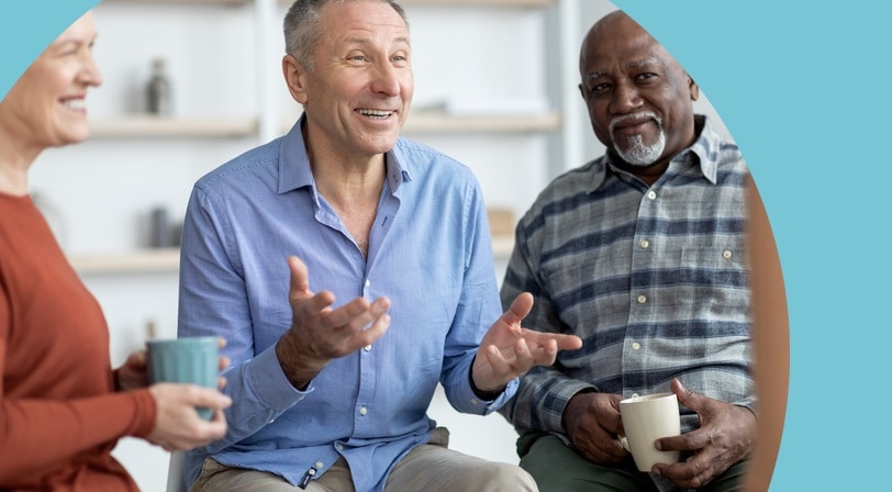 A group of 55+ friends sitting together, talking and holding mugs of coffee.