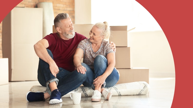 A 55+ couple with moving boxes sitting on a carpet in their new home.