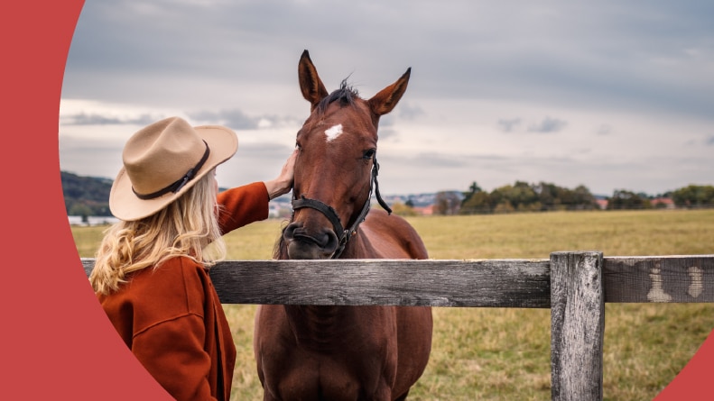 A 55+ woman wearing a cowboy hat and stroking a horse on a ranch in West Texas.