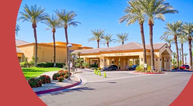 Clubhouse entrance lined with palm trees at Sun City Palm Desert, a 55+ community in Palm Desert, California.