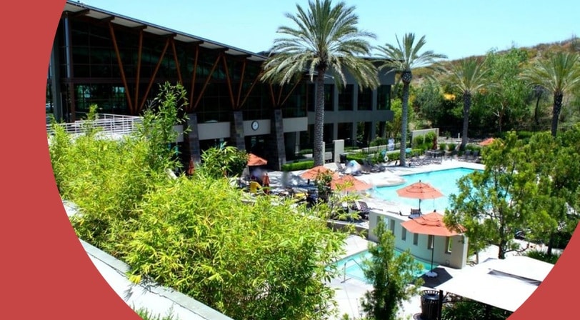 Clubhouse and pool surrounded by palm trees at Trilogy at Glen Ivy, a 55+ community in Corona, California.