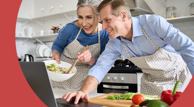 Older couple looking at a recipe on a laptop while cooking.