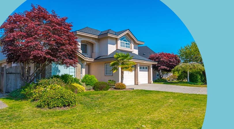 A two-story stucco home with an attached two-car garage, framed by a red-leaf maple and manicured lawn under a clear blue sky.