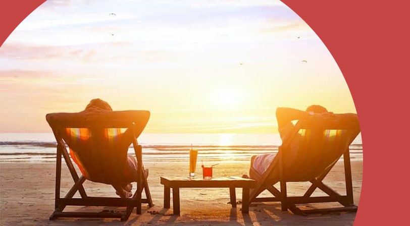 A 55+ couple relaxing in beach chairs watching the sunset over the ocean.