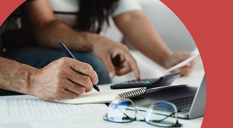 A 55+ couple reviewing financial documents with a calculator, notepad, and laptop.
