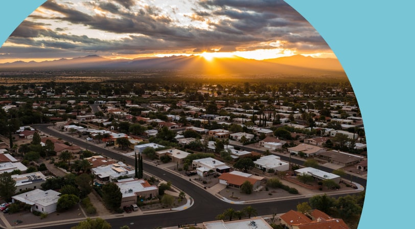 Aerial view of a Green Valley, Arizona neighborhood at sunset, with single-story homes on curving streets and the sun setting behind the Santa Rita foothills.