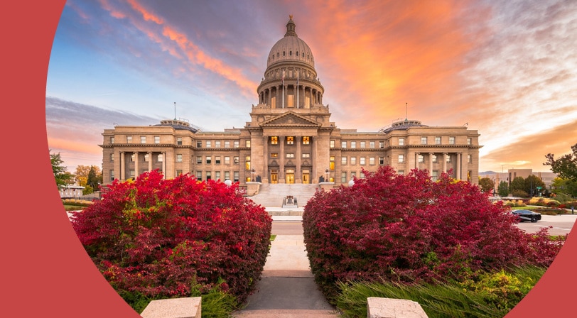The Idaho State Capitol in Boise at sunset, framed by two large shrubs in deep red fall foliage along the walkway.