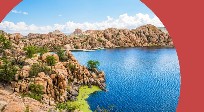 A deep blue lake ringed by weathered granite boulder formations under a partly cloudy sky.