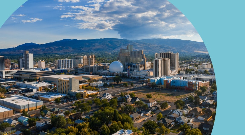 Aerial view of downtown Reno, Nevada, showing hotel towers and tree-lined residential streets with the Sierra Nevada foothills in the background.