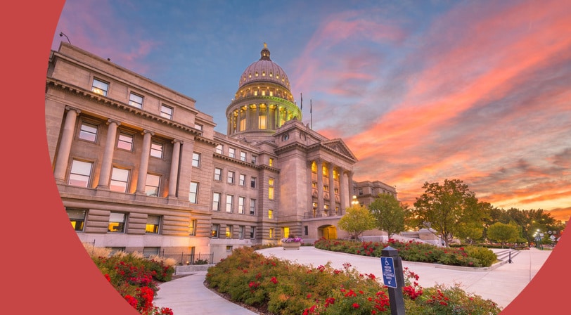 The Idaho State Capitol building in Boise at sunset, with its illuminated dome and rose gardens along the front walkway.