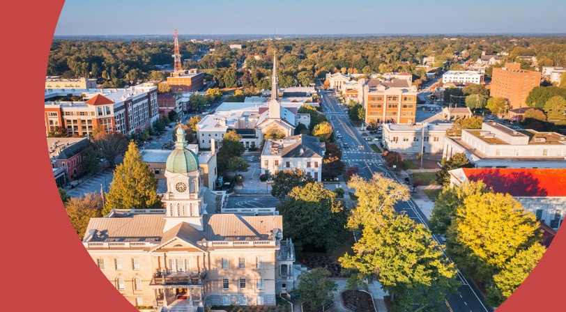 Aerial view of downtown Athens, Georgia at sunrise, with the domed City Hall clock tower, a white church steeple, and tree-lined streets stretching toward the horizon.