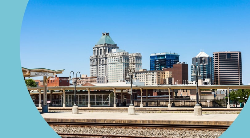 The downtown Greensboro, North Carolina skyline seen from the train station platform, with the historic Jefferson Standard Building rising above the depot canopy.