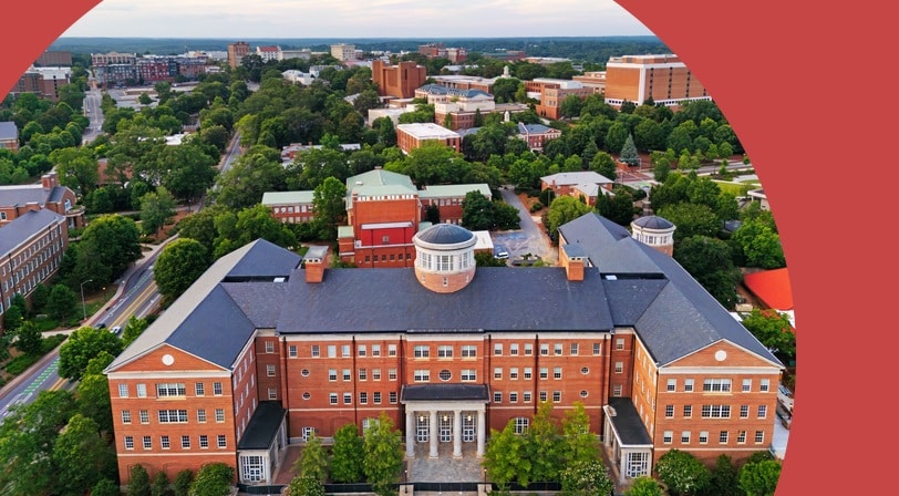 Aerial view of the University of Georgia campus in Athens, with a brick academic building topped by a white cupola surrounded by dense tree cover.