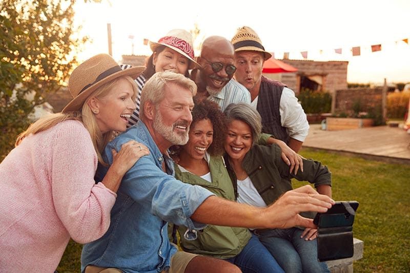Mature friends in a 55+ community sitting around a fire and taking a selfie.