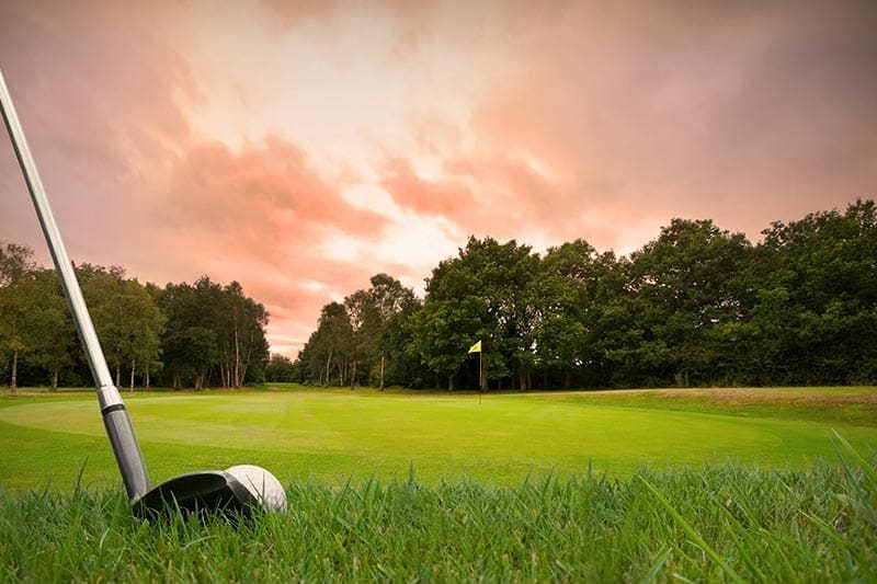 Chipping a golf ball onto the green with golf club at sunset.