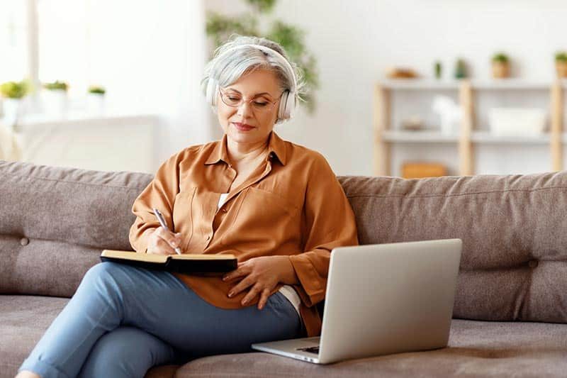 elderly-female-headphones-writing-in-notebook