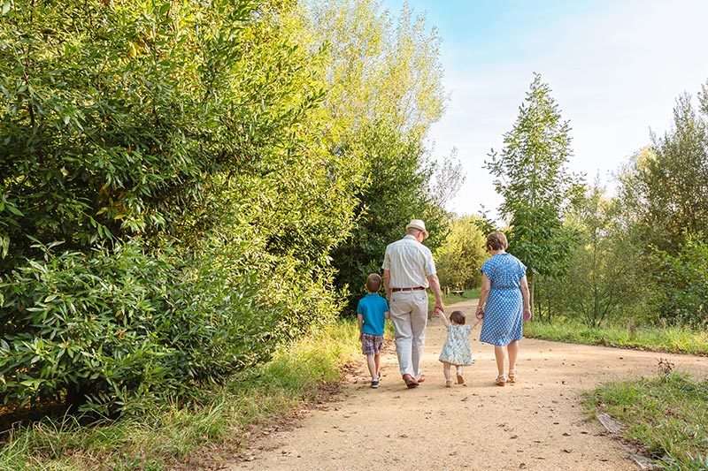 Back view of grandparents and grandchildren walking on a nature path in a 55+ community.