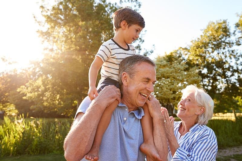 Grandfather giving his grandson a ride on his shoulders in a park in a 55+ community.