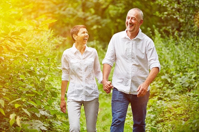 A happy senior couple taking a walk during the summer in a forest.