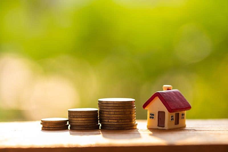 A small model house beside a stack of coins.