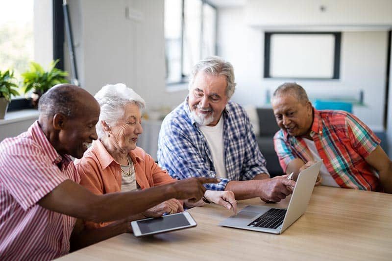 Happy senior men and woman using a laptop while sitting at table in a nursing home.