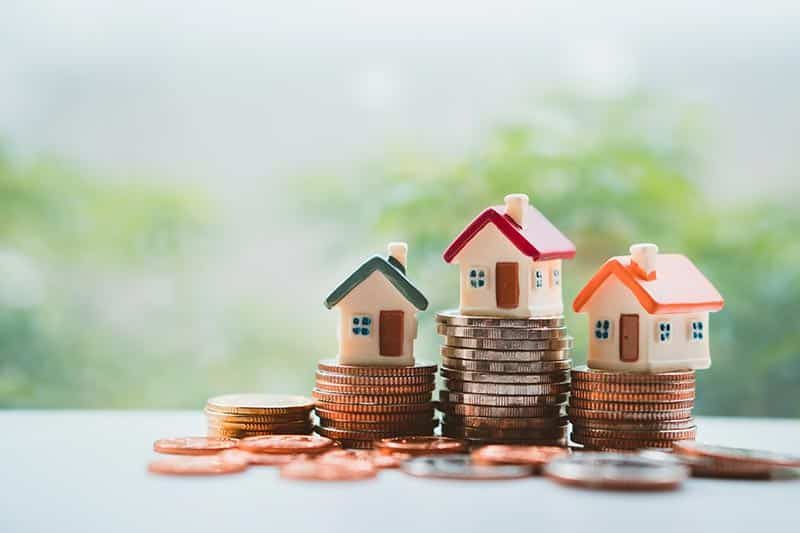 Miniature colorful houses sitting on a on stack coins on a table.