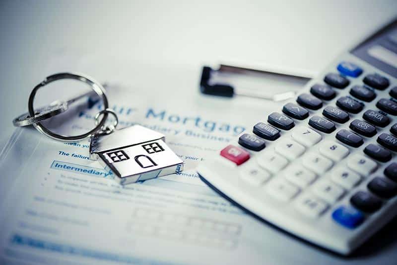 A calculator beside a key with a house keychain on a mortgage application.