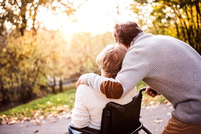 A senior couple with the woman in a wheelchair on a waling path in autumn.