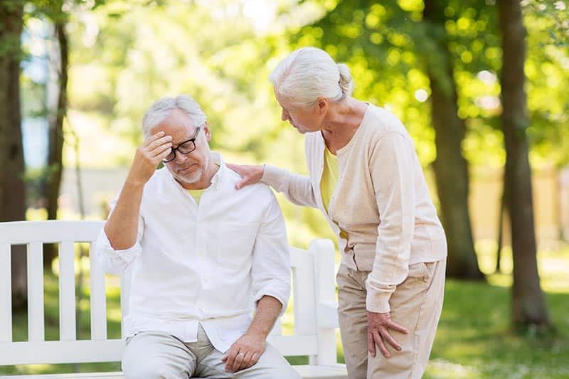 A senior woman comforting a stressed senior man on a bench outside.
