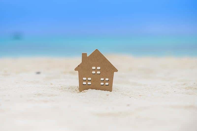 Small home model on sand beach with blue sky background.