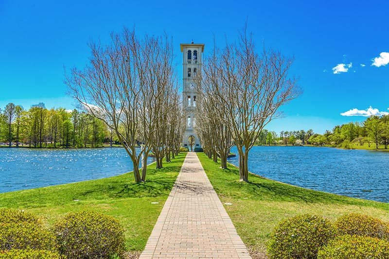 View down a paved walkway beside Furman Swan Lake and Bell Tower in Greenville, South Carolina.