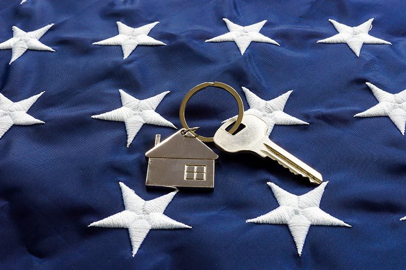 A key with a house keychain on top of an American flag.